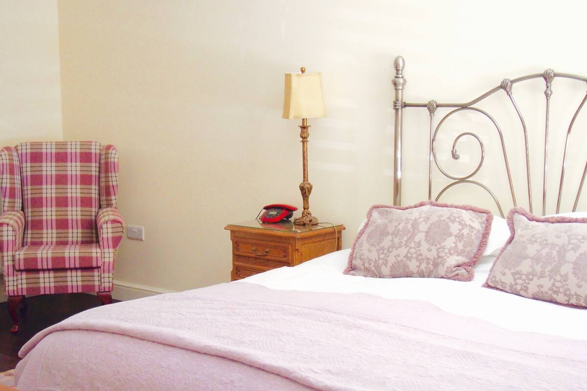 A bedroom with a bed, a nightstand with a lamp, a chair, and a telephone.