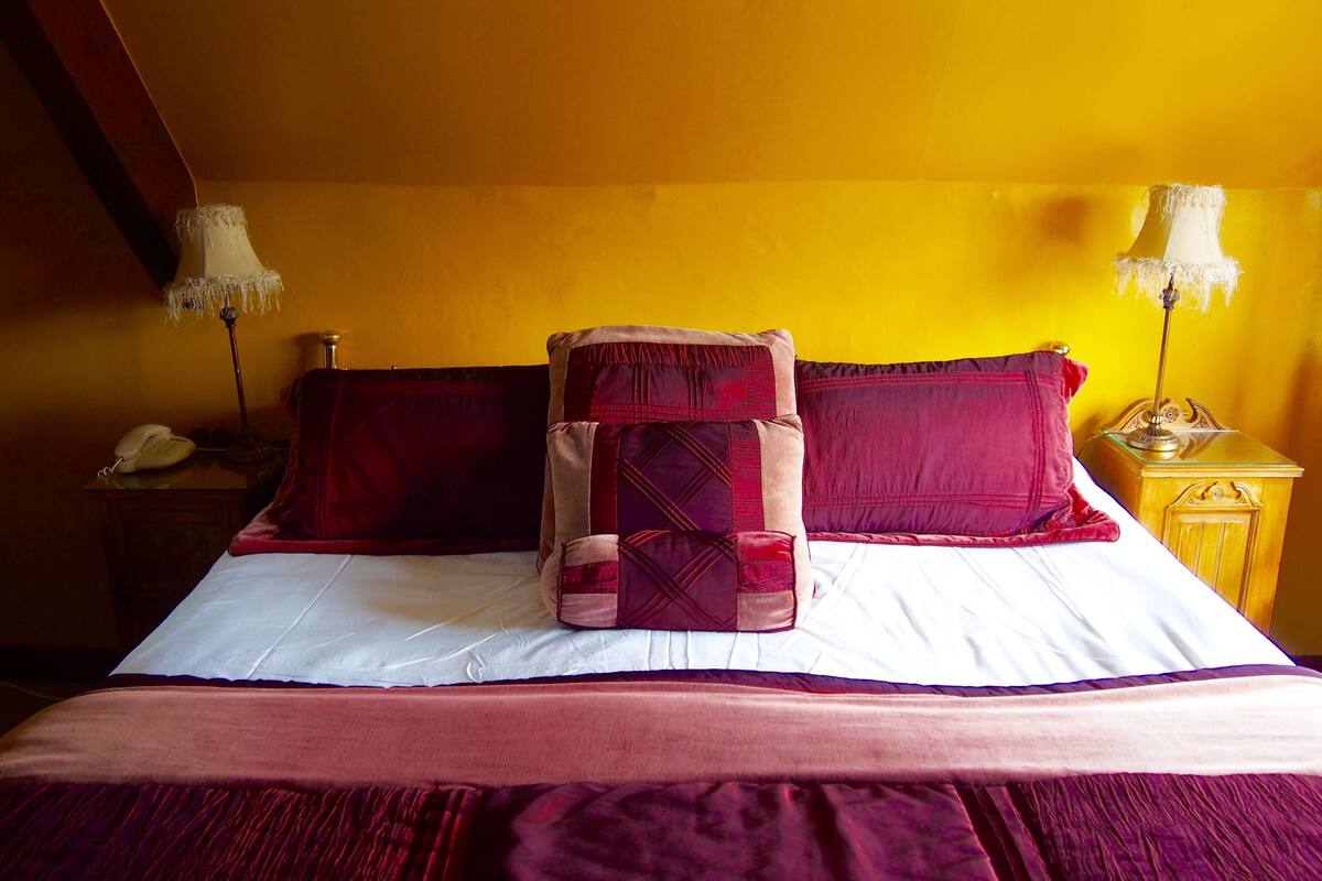A bed with a white sheet and a red and beige blanket. There are two lamps on either side of the bed.
