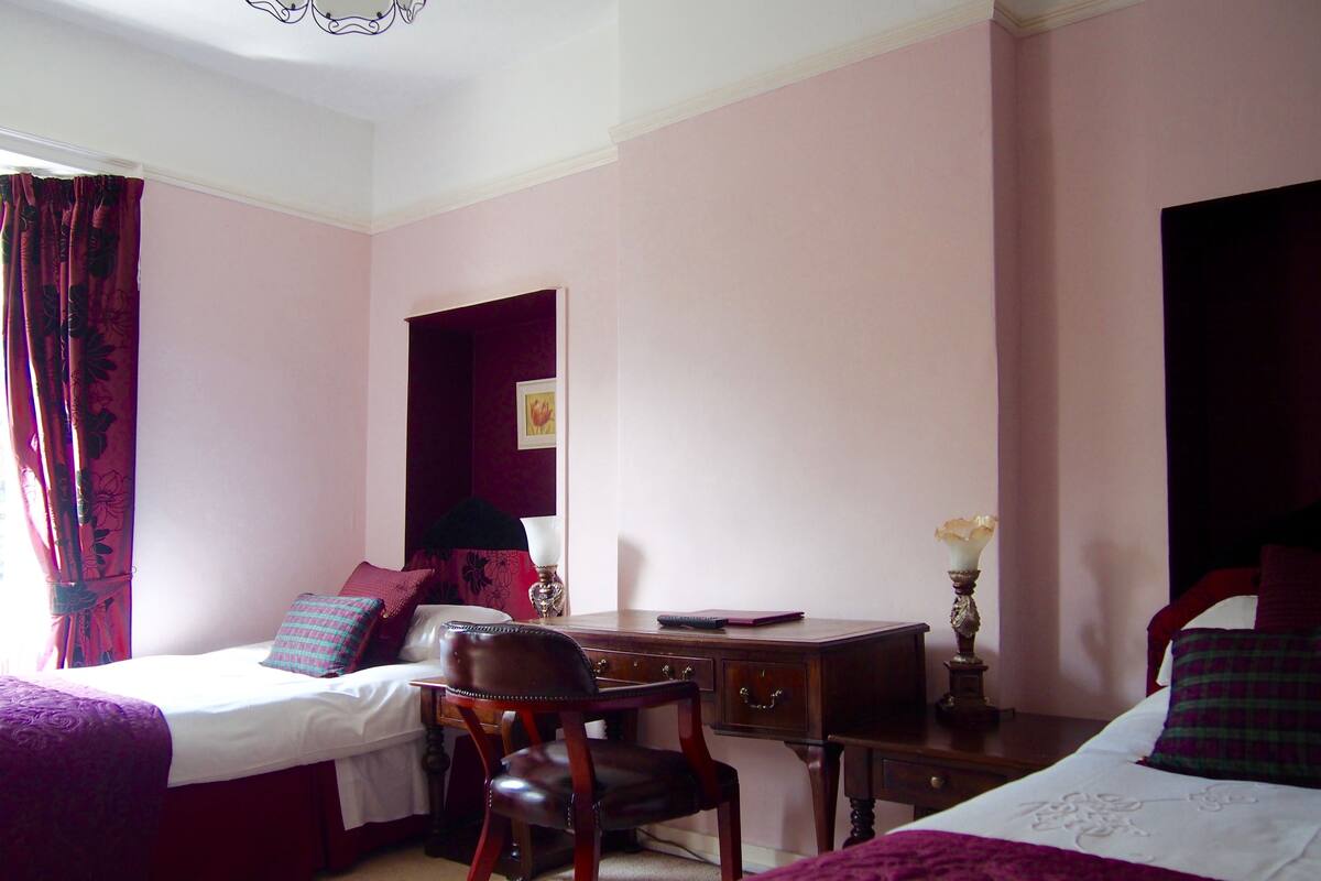 A room with two beds, a desk, a chair, and a window with curtains.