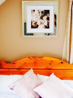 Un dormitorio con cabecera de madera, un cuadro en la pared y una cama con almohadas blancas y rosas.