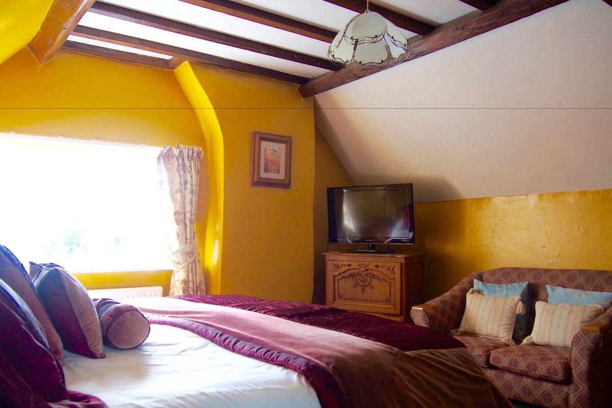 A bedroom with a bed, a television on a wooden cabinet, a sofa, and a window with curtains.