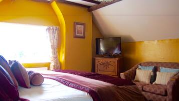 A bedroom with a bed, a television on a wooden cabinet, a sofa, and a window with curtains.