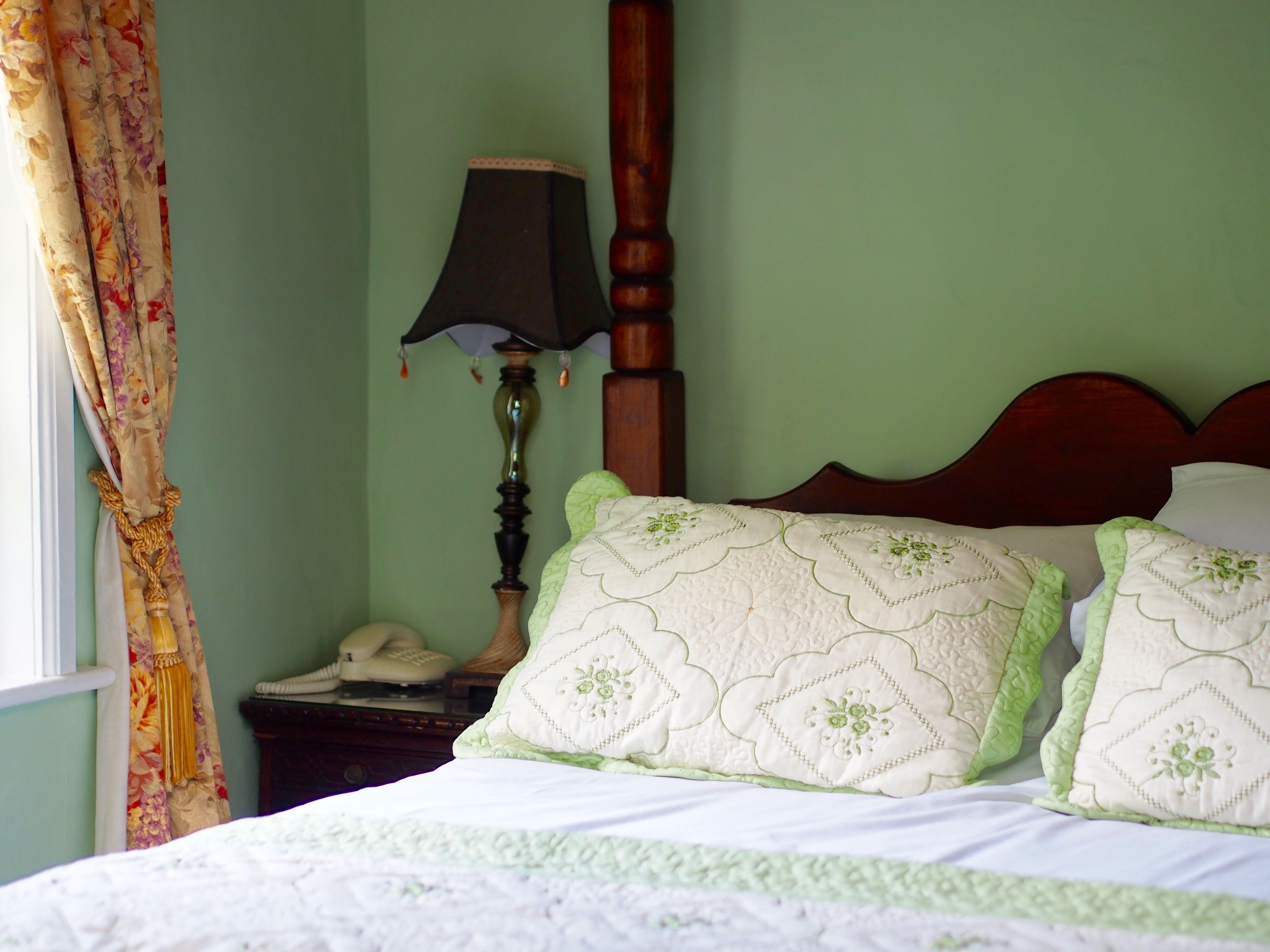 A bedroom with a bed, two pillows, a nightstand, a lamp, and a curtain.