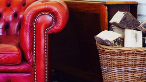 Un fauteuil en cuir rouge, une lampe, un vase avec des fleurs violettes et un panier en osier rempli de bûches.