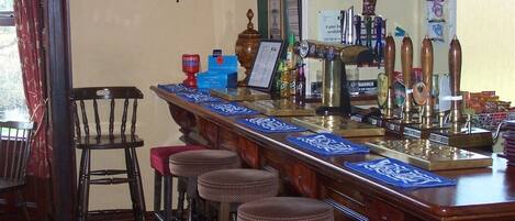 A bar area with stools, a bar counter, and a clock on the wall.