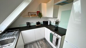 A compact kitchen with white cabinets, a black countertop, a microwave, a kettle, and a toaster. - New Forest Lodge (Salisbury)