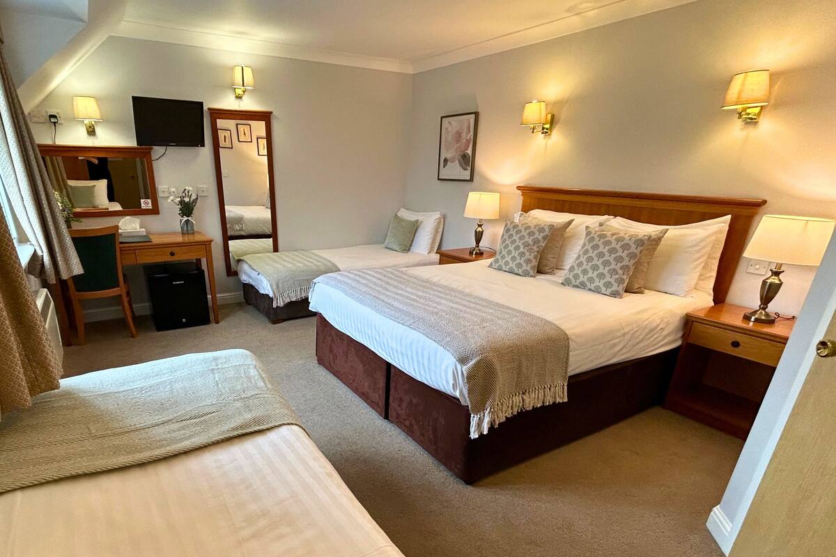 A hotel room with two beds, a desk, a chair, a TV, and wall-mounted lamps.