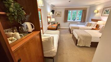 A hotel room with two beds, a small desk, a mirror, a window with curtains, and a plant.
