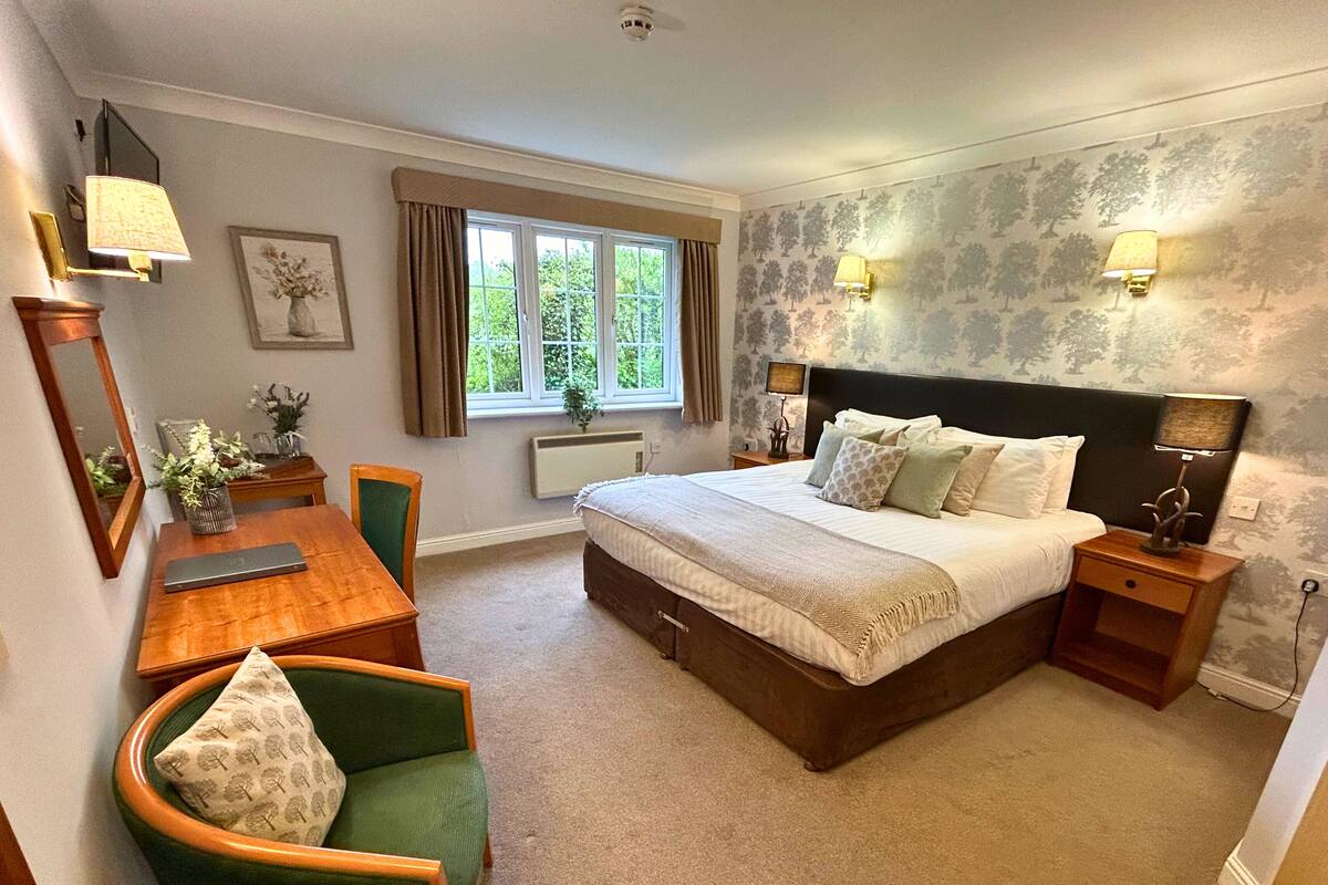 A bedroom with a bed, bedside tables, a desk, a chair, a window, and a mirror.