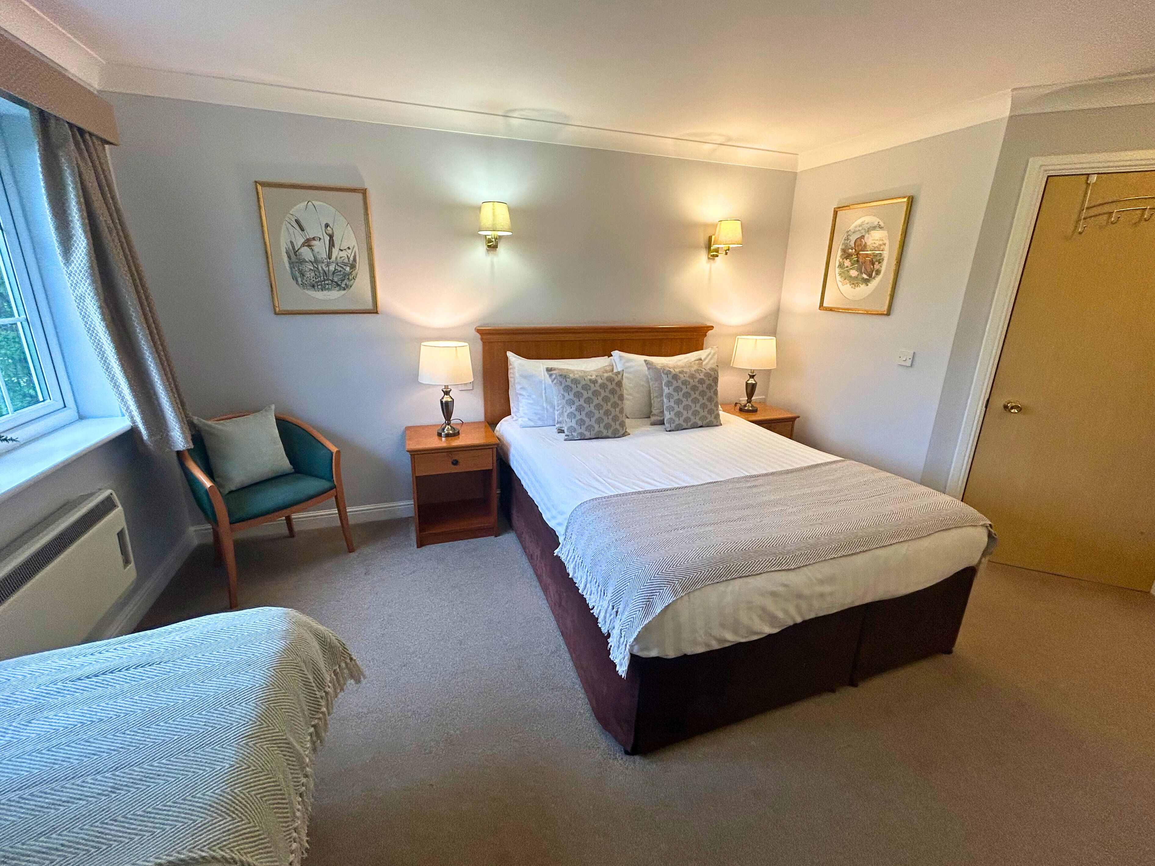 A hotel room with a large bed, two bedside tables with lamps, a chair, and two framed pictures on the walls.