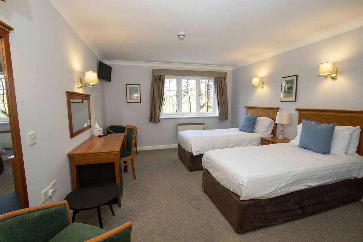A hotel room with two beds, a desk, a chair, a TV, and a window with curtains.