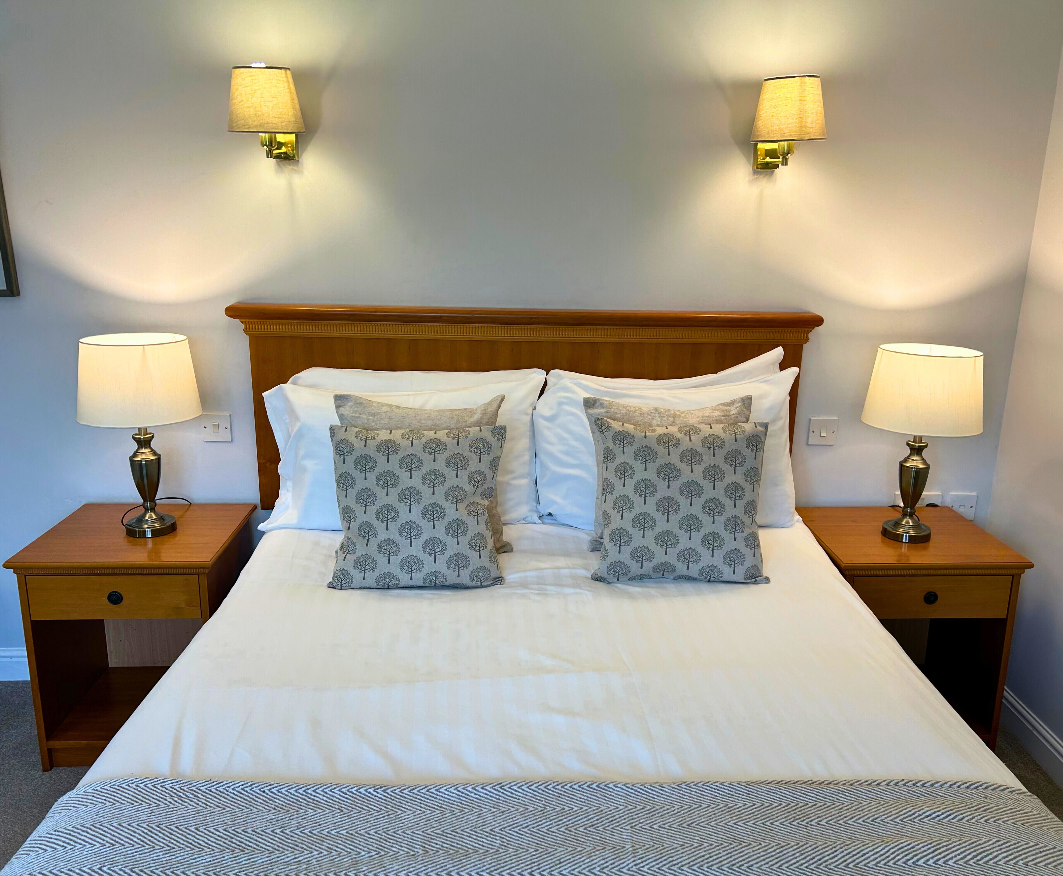 A neatly made bed with two matching pillows, two bedside lamps, and a wooden headboard.