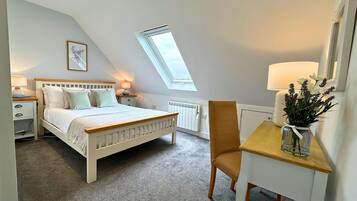 Un dormitorio con techo inclinado, cama, escritorio y silla.