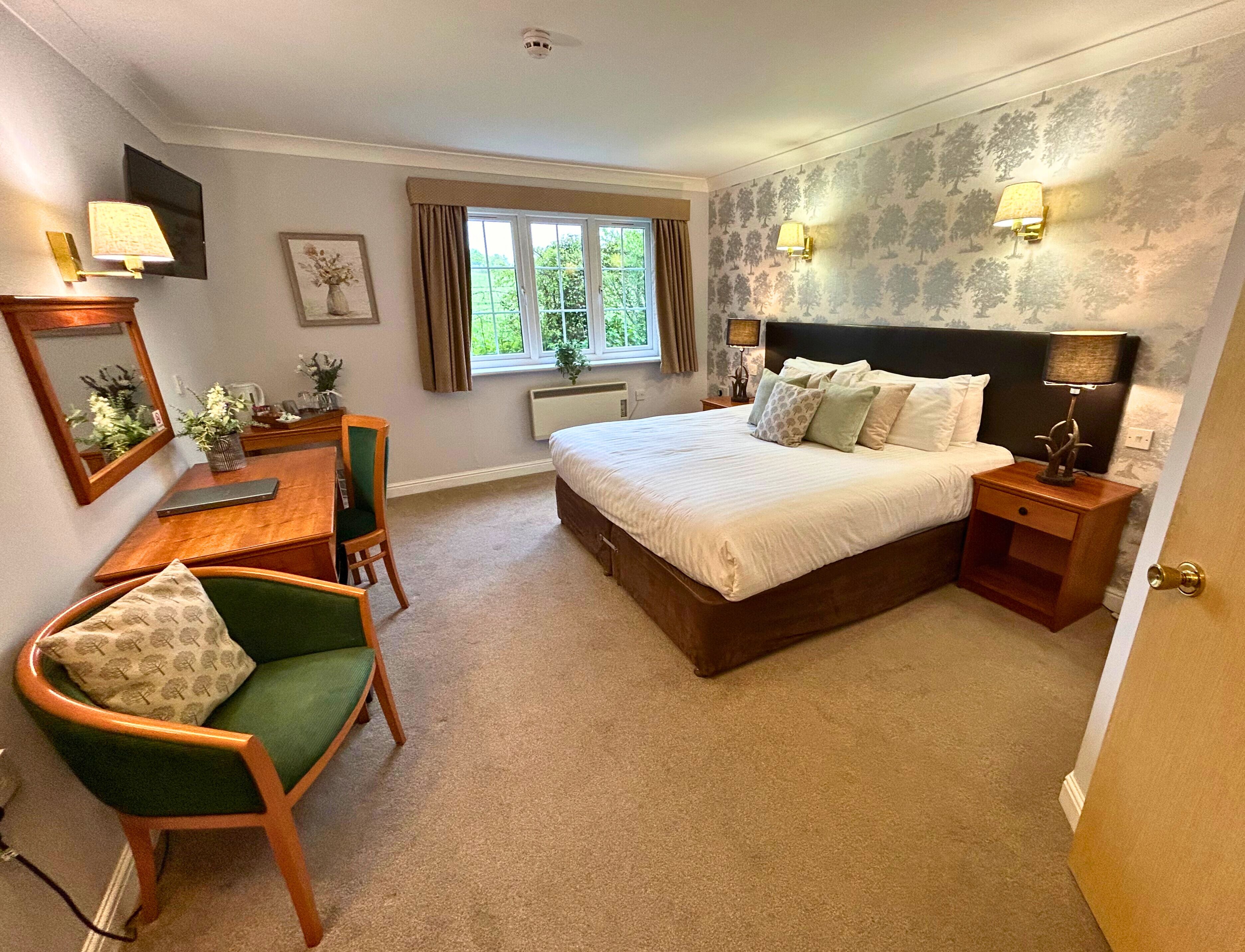 A bedroom with a large bed, bedside tables, a desk, a chair, and a window with curtains.