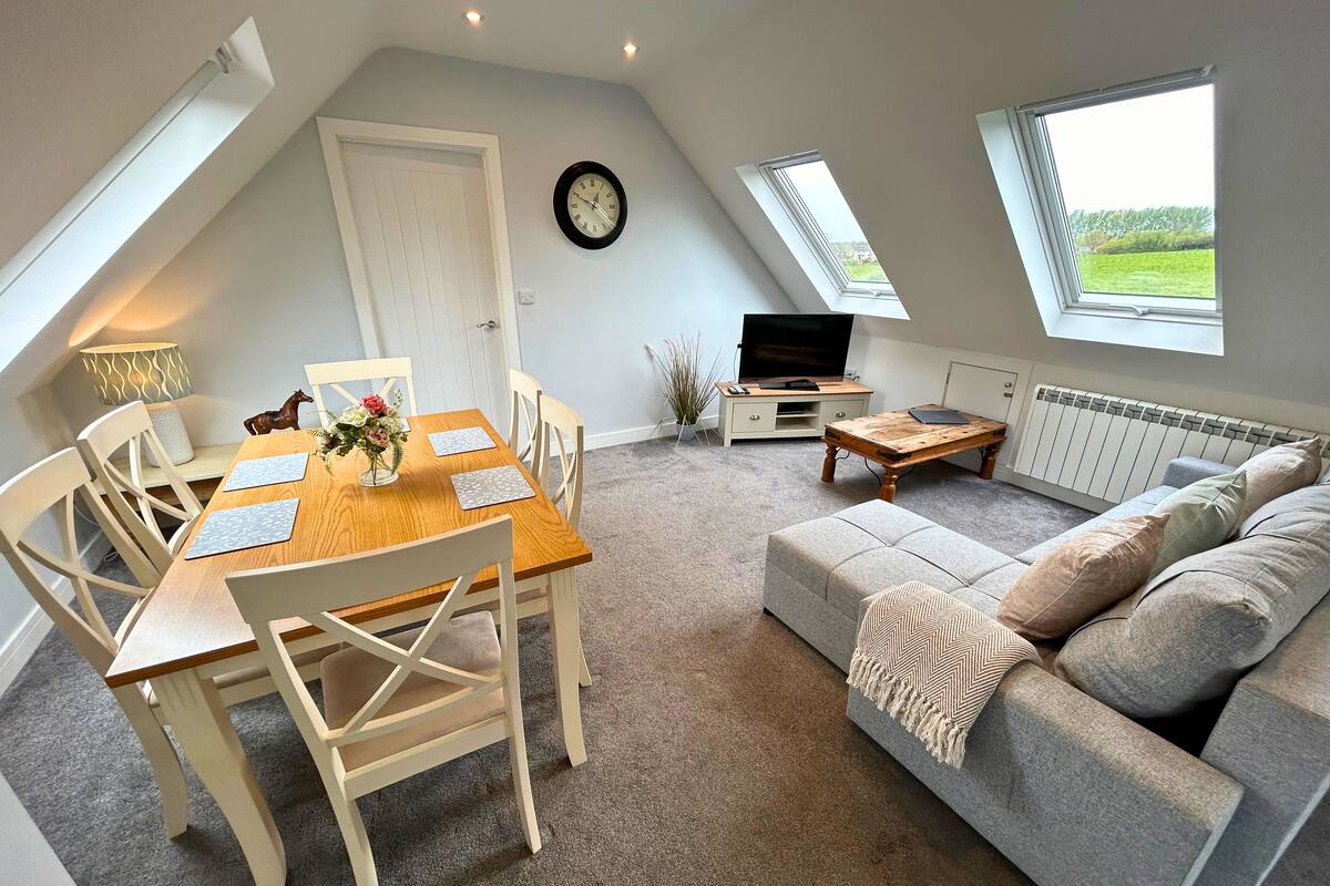A cozy living room with a dining area, a sofa, a TV, and a clock on the wall.