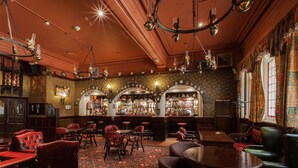 A bar area with leather seating, a patterned carpet, and a bar counter with bottles. - Scarisbrick Hotel (Southport)