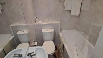 A modern bathroom with a sink, two toilets, and a bathtub.
