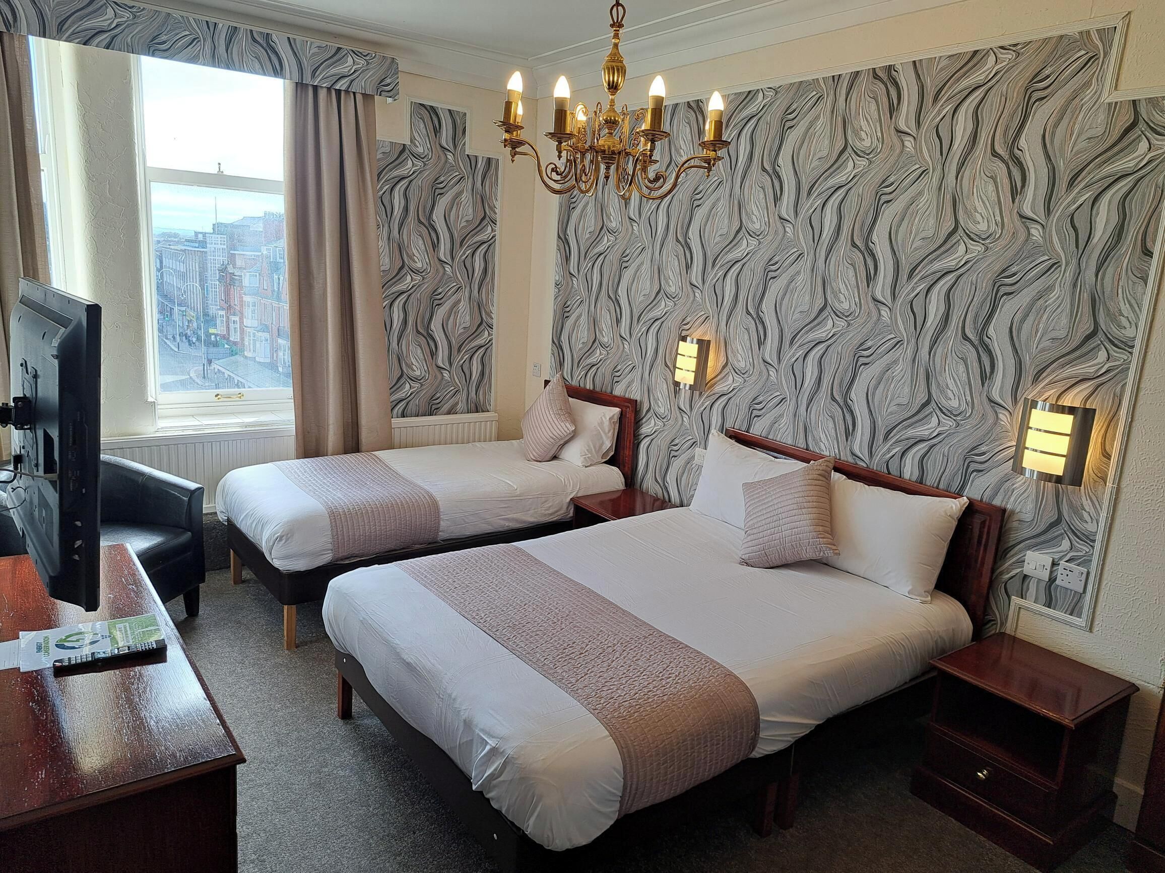 A hotel room with two beds, a TV, a desk, and a view of the city.