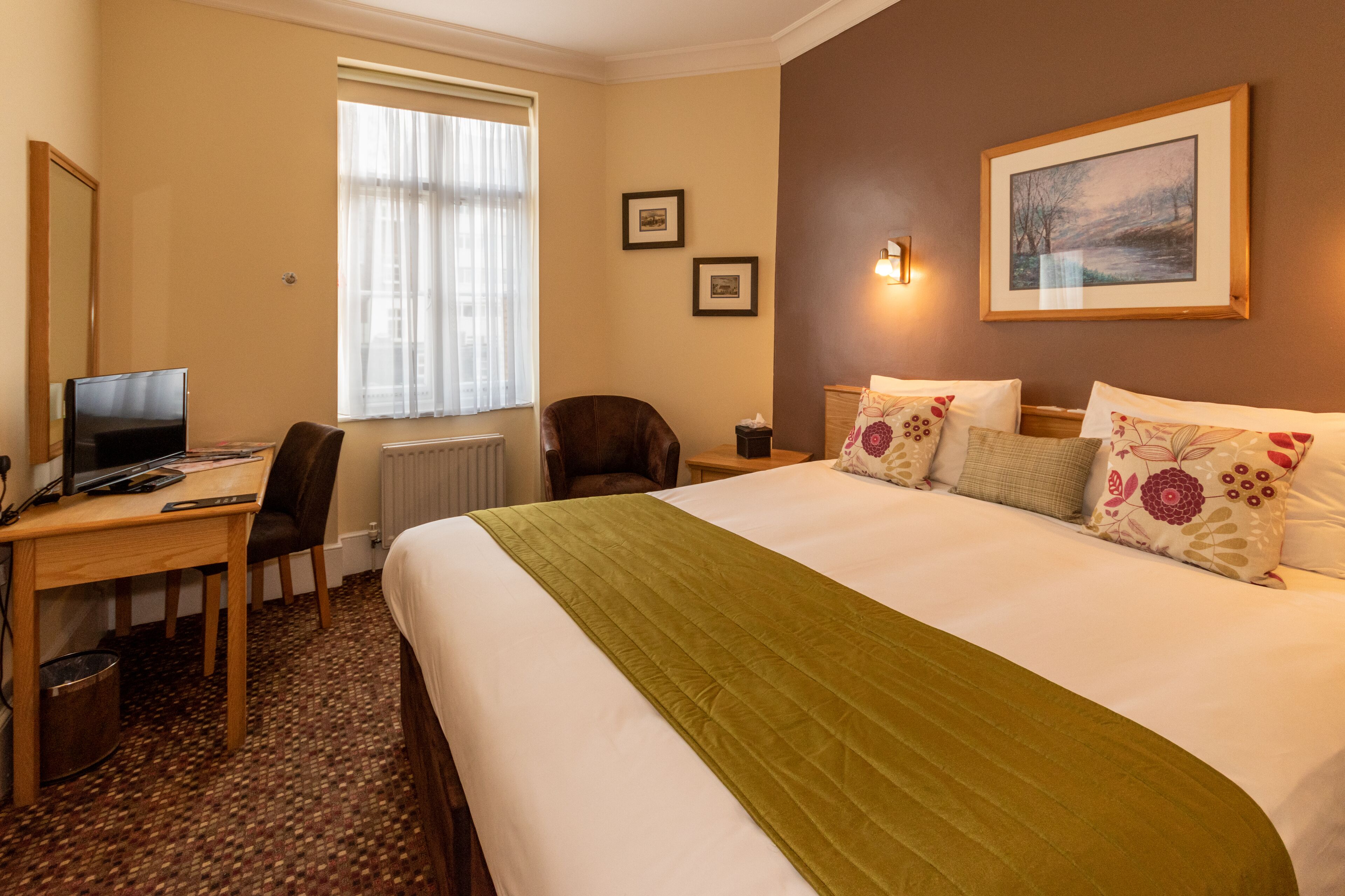 Habitación de hotel con una cama grande, un escritorio con computadora, una silla y una ventana con cortinas.