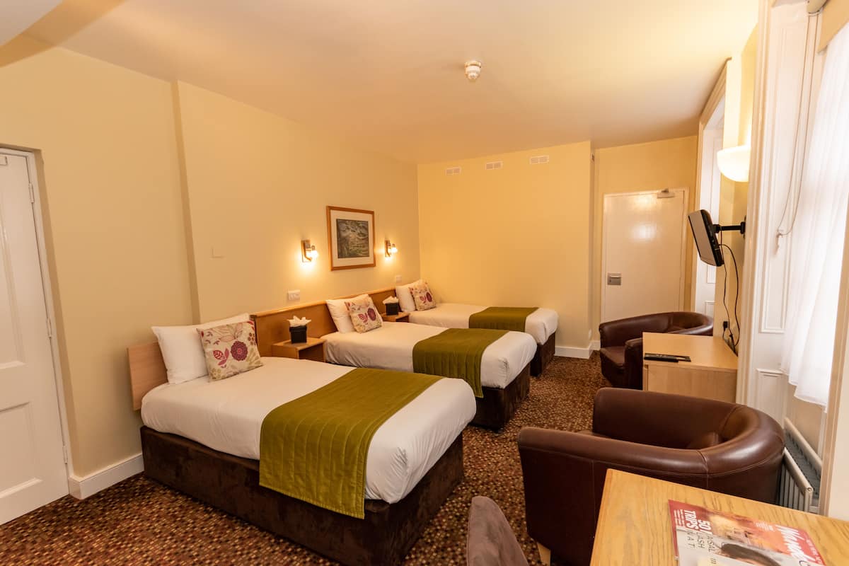 A hotel room with three beds, a desk, a chair, and a lamp.