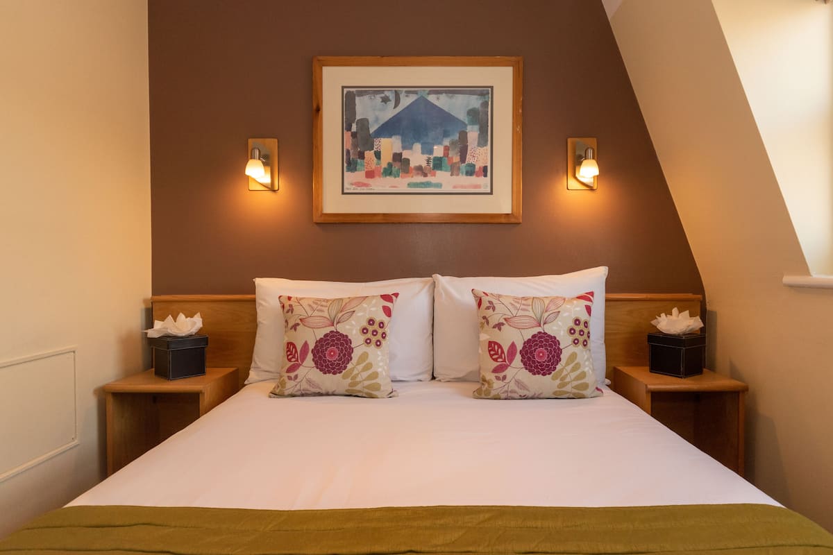 A hotel room with a bed, two nightstands, a framed picture on the wall, and two wall-mounted lights.