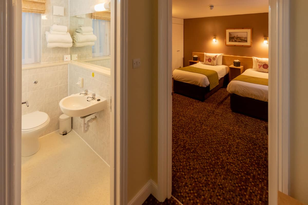 A hotel room with a bathroom, two beds, and a carpeted floor.