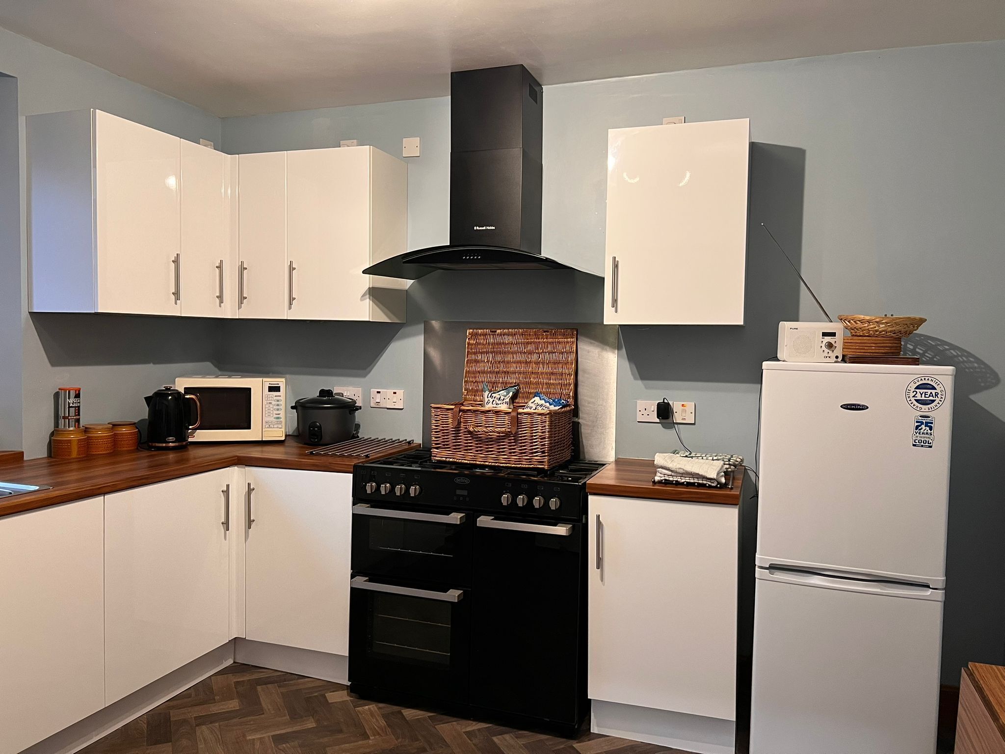 Una cocina compacta con armarios blancos, una estufa negra, un microondas y un refrigerador.