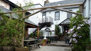 A courtyard with wooden tables and chairs, potted plants, and a wooden pergola. - The Falcon Hotel (Bromyard)