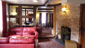 A cozy room with a red leather sofa, a brick fireplace, and a patterned carpet. - The Falcon Hotel (Bromyard)