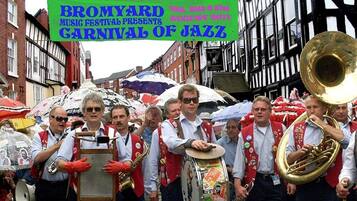 A group of musicians in traditional attire, carrying instruments, and a banner for the Bromyard Music Festival.