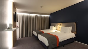 A hotel room with two beds, a desk, a TV, and a large window with curtains. - Knowsley Inn & Lounge (Liverpool)