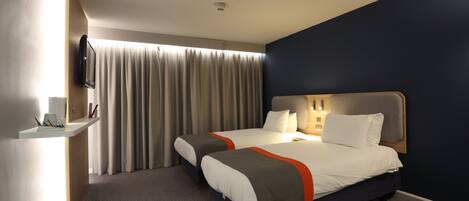 A hotel room with two beds, a desk, a TV, and a large window with curtains.