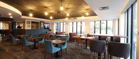 A spacious indoor area with tables and chairs, large windows, and a patterned carpet.