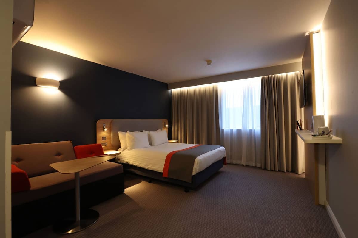 A hotel room with a bed, a sofa, a small table, and a TV.
