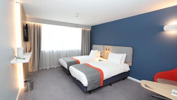 A hotel room with two beds, a desk, a chair, a TV, and a window with curtains.