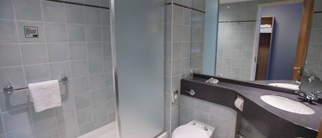 Un baño moderno con ducha envuelta en vidrio, inodoro blanco y tocador doble.
