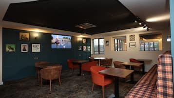 A restaurant with a cozy interior, featuring a mix of wooden and upholstered furniture, a patterned carpet, and wall-mounted artwork.