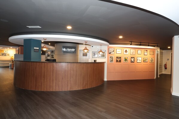 A reception area with a curved wooden reception desk, framed artwork on the walls, and a sign that reads "Knowley".