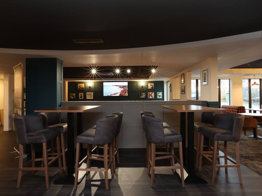 A modern bar area with high stools, a large TV screen, and framed pictures on the wall.