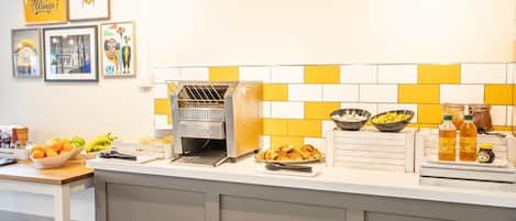 A breakfast bar with a coffee machine, fruit bowls, and condiments.