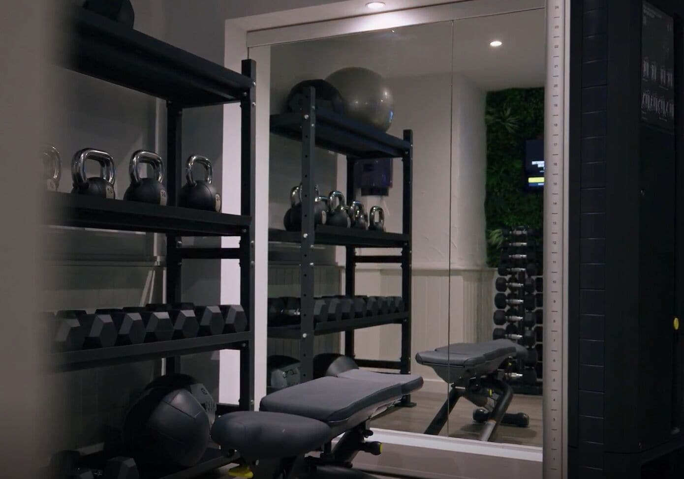 A gym with weightlifting equipment, a bench, and a mirrored wall.