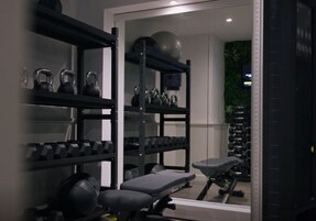 Un gimnasio con equipo de levantamiento de pesas, una banca y un espejo grande.
