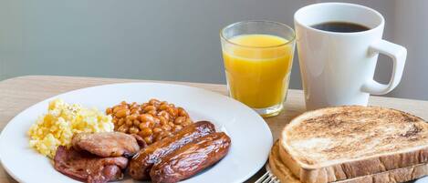 A plate with eggs, sausages, beans, toast, and a glass of orange juice.