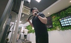 Ett gym med träningsutrustning, en väggmonterad TV och en person som använder en motionscykel.