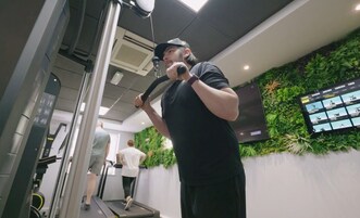 Uma academia com equipamentos de exercício, uma televisão na parede e uma pessoa usando uma bicicleta ergométrica.
