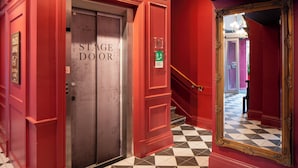 Ein Hotelkorridor mit einer Bühnentür, einem Spiegel und einem Schachbrettmuster-Boden.