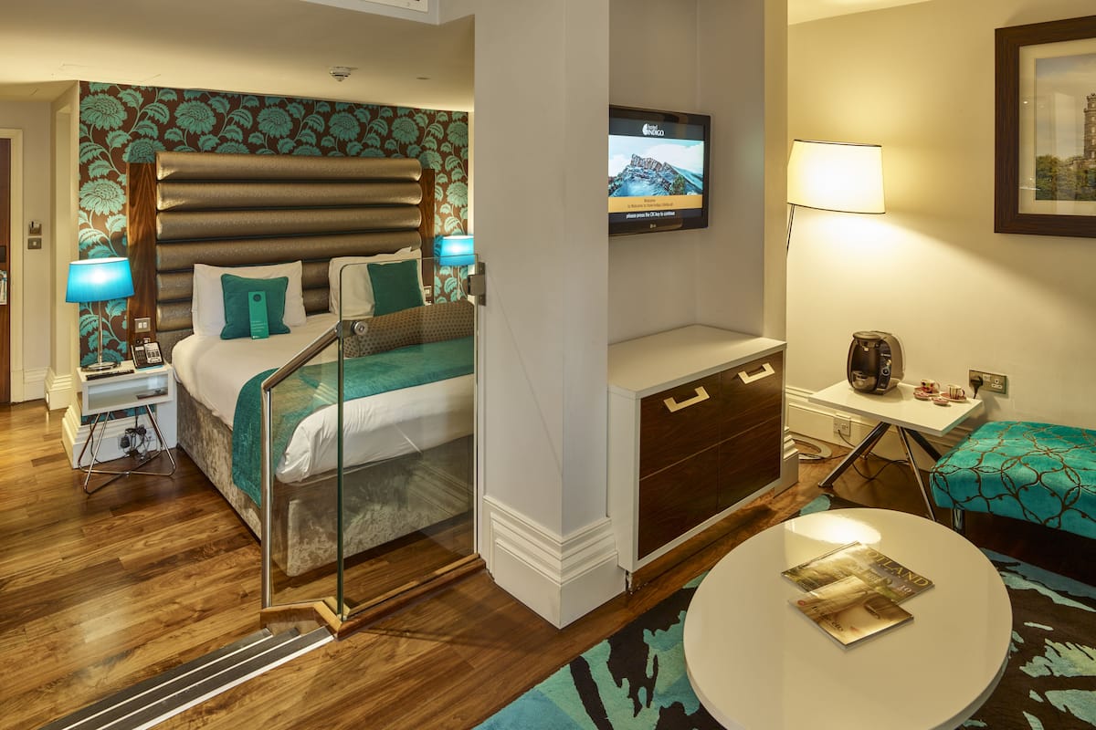 A hotel room with a bed, bedside table, TV, desk, chair, and a round table.