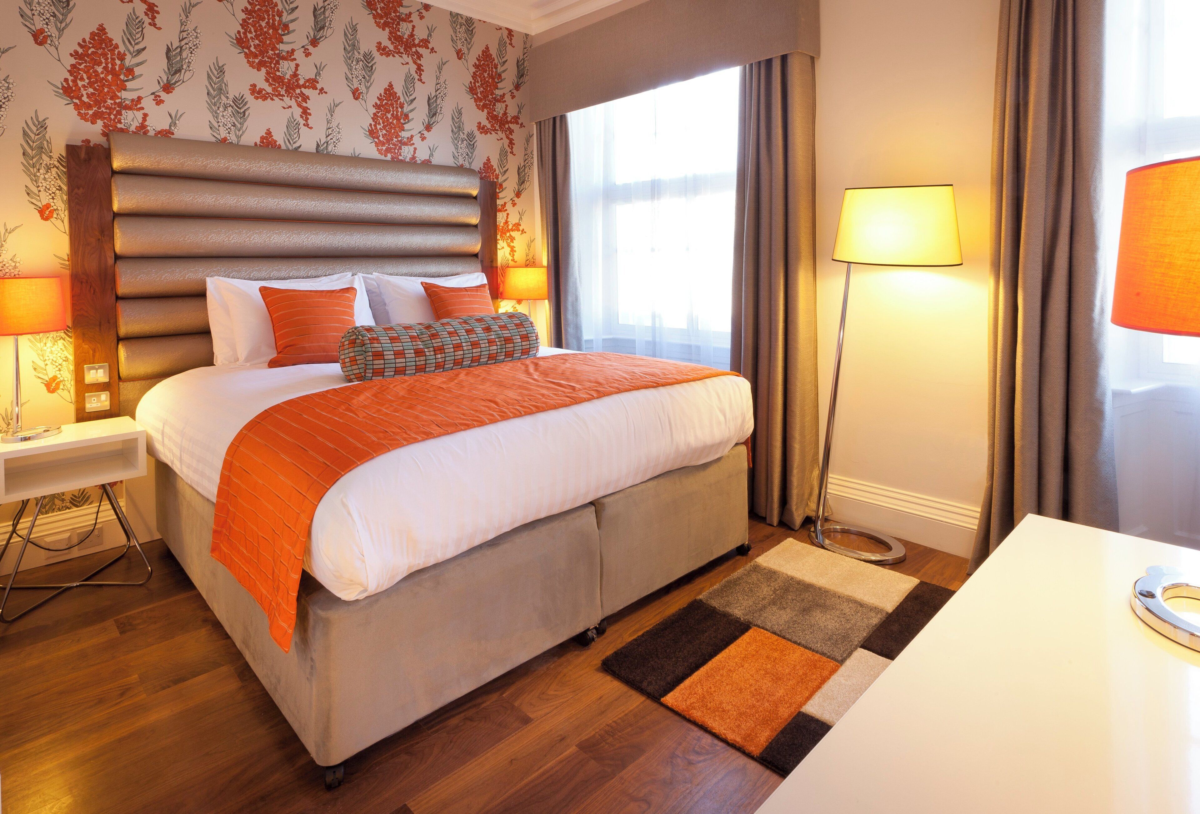 A hotel room with a large bed, a bedside table, a desk, and a window with curtains.