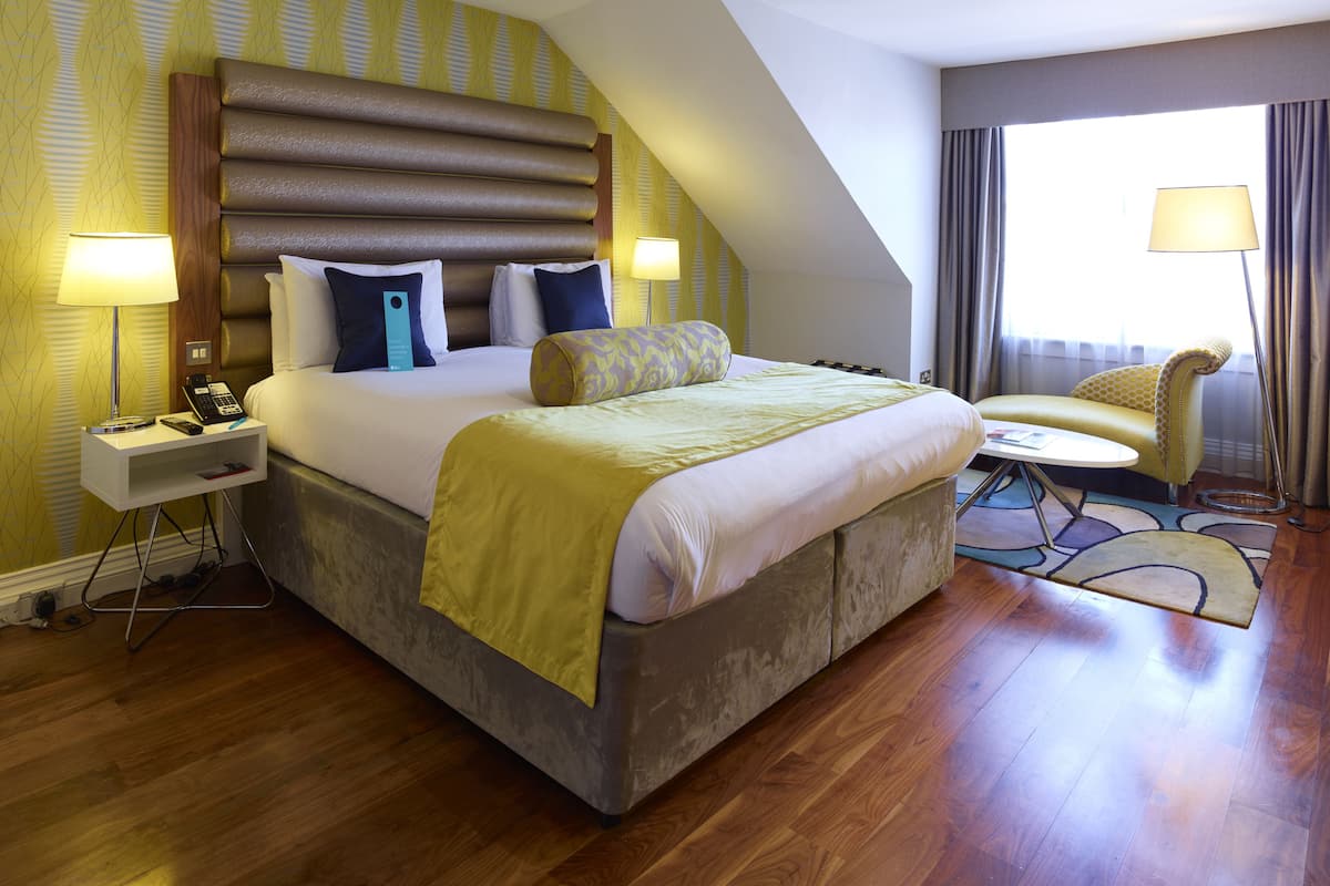 A hotel room with a large bed, bedside lamps, a desk, and a chair.