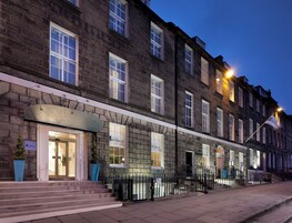 A hotel with a stone facade, multiple windows, and a staircase leading to the entrance.